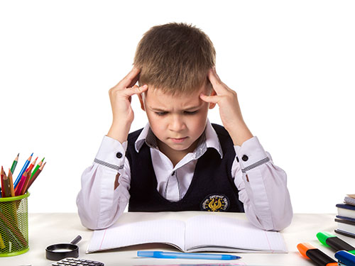 Frustrated child holding hands against his head while staring at school work